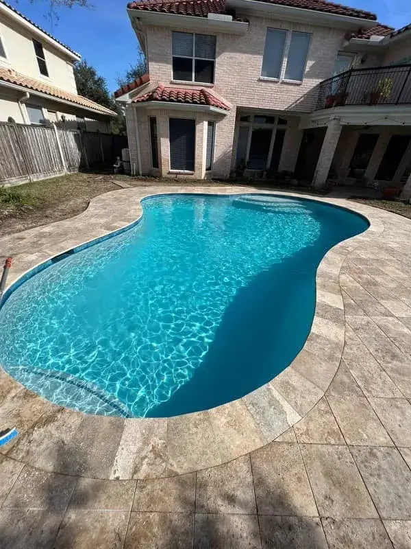 Freeform curved swimming pool with travertine pool deck in an East Texas backyard