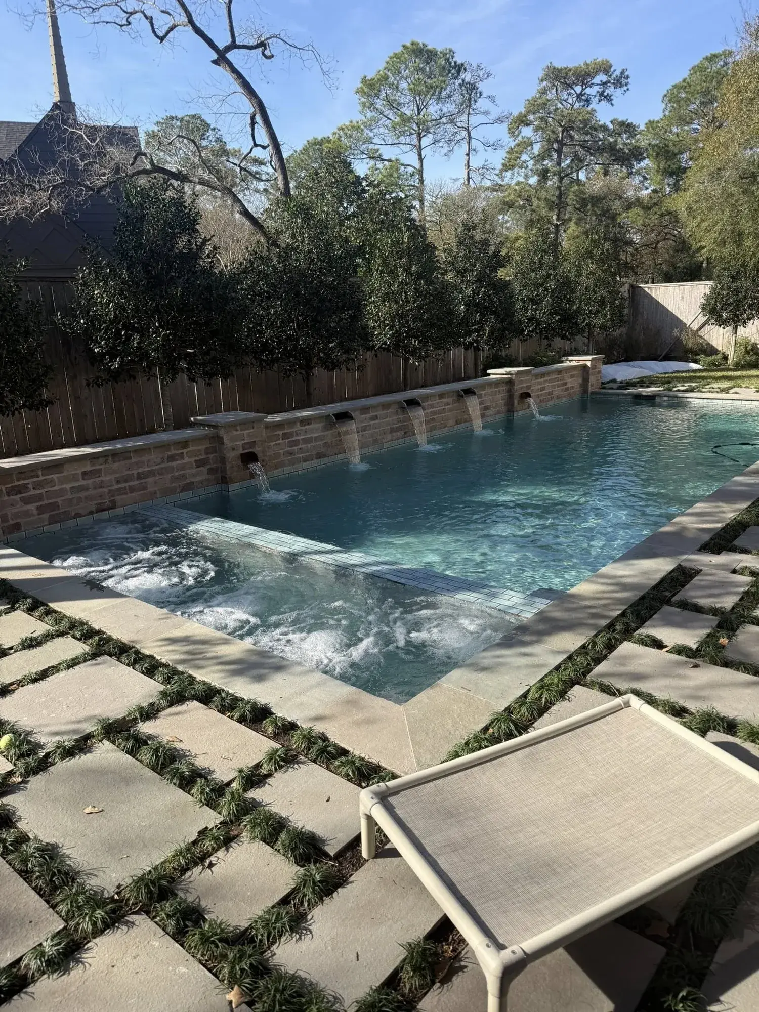 Modern rectangular pool with three sheer descent waterfalls from a raised wall, built by Sam Houston Pools and Outdoors
